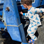 Child climbing on a blue tractor wearing a blue tractor design pajama set with a clear sky background