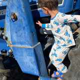 Child climbing on a blue tractor wearing a blue tractor design pajama set with a clear sky background