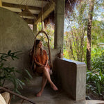 Woman sitting in a hanging chair on a tropical patio with lush greenery.