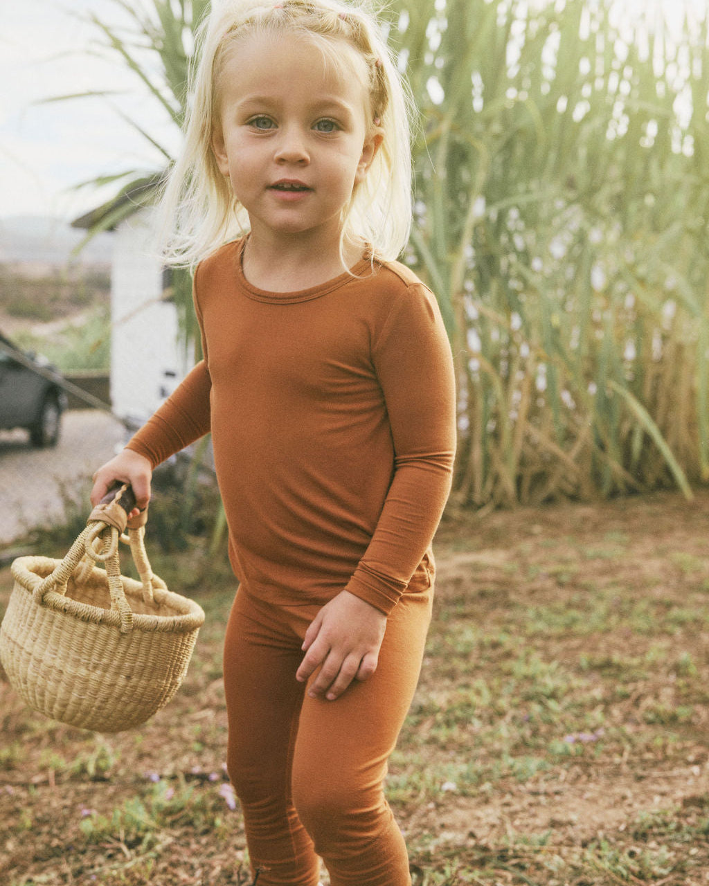 Child in a Canyon Clay Two-Piece holding a woven basket outdoors.