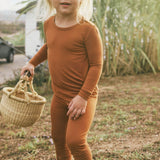 Child in a terracotta-colored outfit pajama set holding a woven basket outdoors.