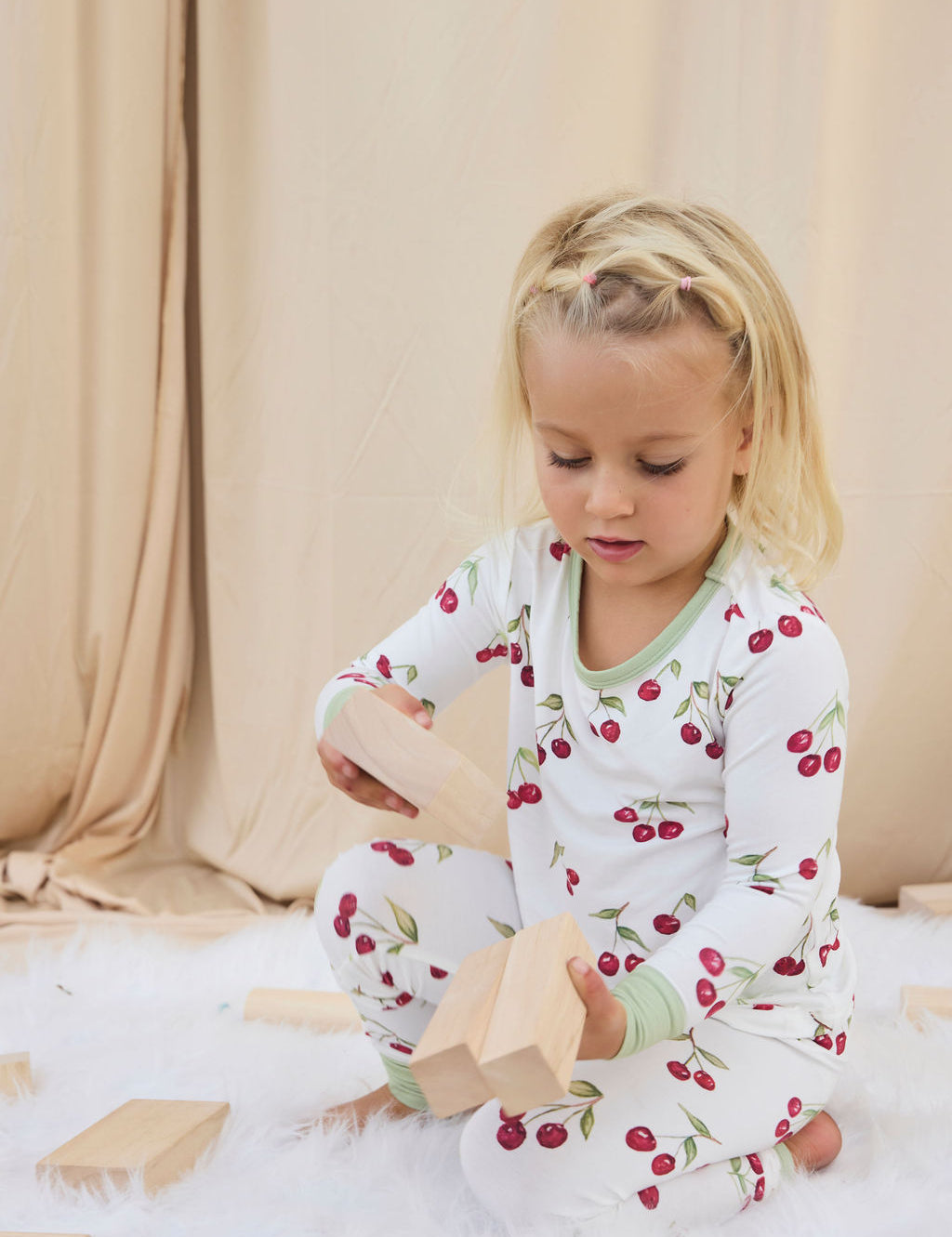 Child playing with wooden blocks wearing a white two-piece pajama with hand-painted red cherries.