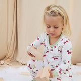 Child playing with wooden blocks wearing a white two-piece pajama with hand-painted red cherries.
