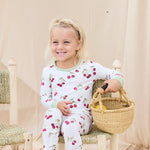 Child wearing hand-painted cherry-patterned pajamas sitting on a wooden stool holding a basket.
