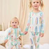 Two children wearing matching hand-painted pajamas with a colorful pastel surfboard pattern in a cozy room.