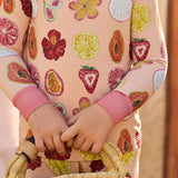 Child wearing a colorful hand-painted fruit-patterned two-piece pajama set holding a woven basket.