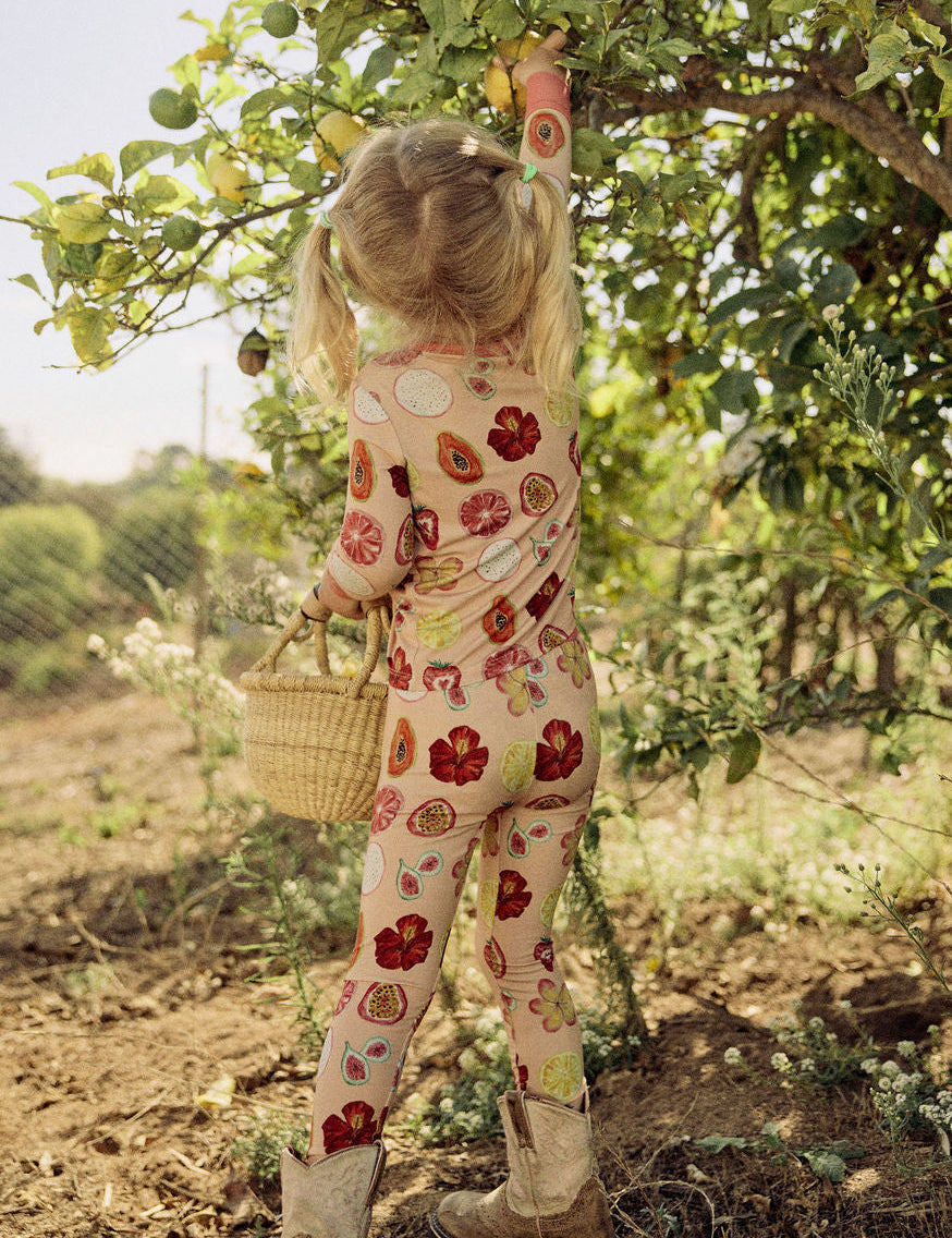Child in a hand-painted floral pajama set picking lemons from a tree in an orchard.