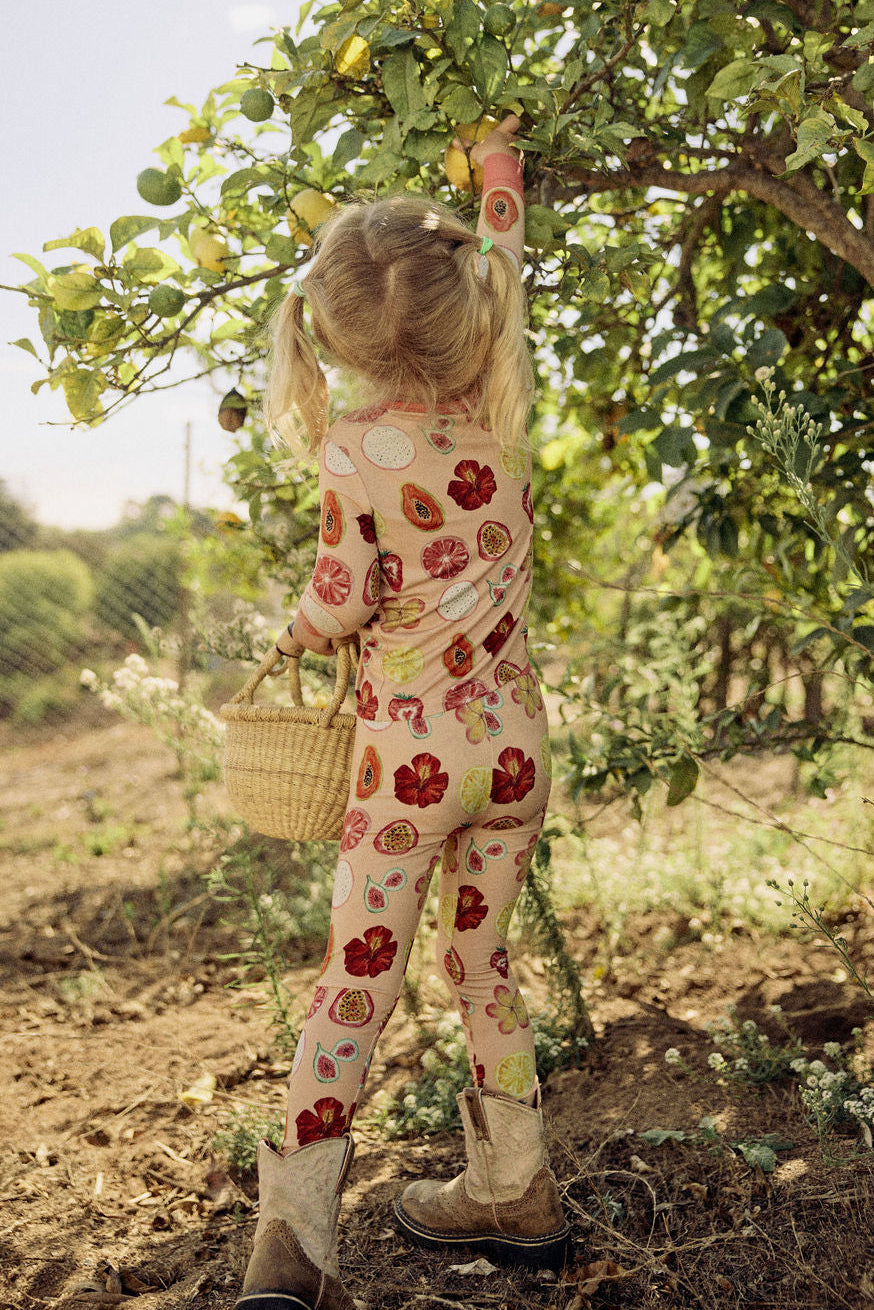 Child in a hand-painted floral pajama set picking lemons from a tree in an orchard.