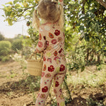 Child in a hand-painted floral pajama set picking lemons from a tree in an orchard.