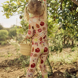 Child in a hand-painted floral pajama set picking lemons from a tree in an orchard.
