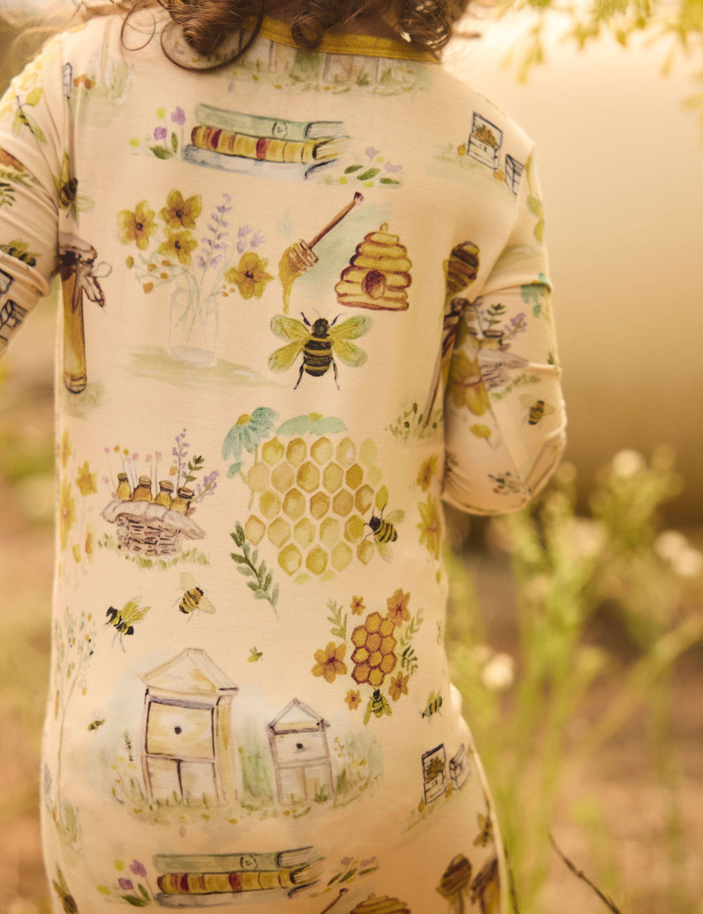 Child wearing a onesie with bee and honeycomb patterns in a natural setting