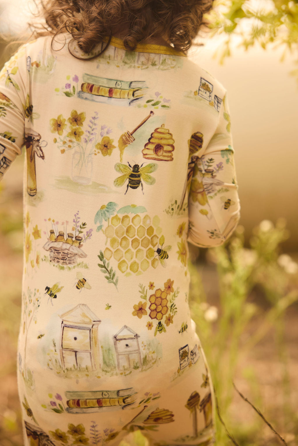Child wearing a onesie with bee and honeycomb patterns in a natural setting