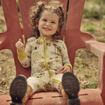 Child sitting on a red chair outdoors wearing a hand-painted honey and bees themed pajama with a blurred natural background