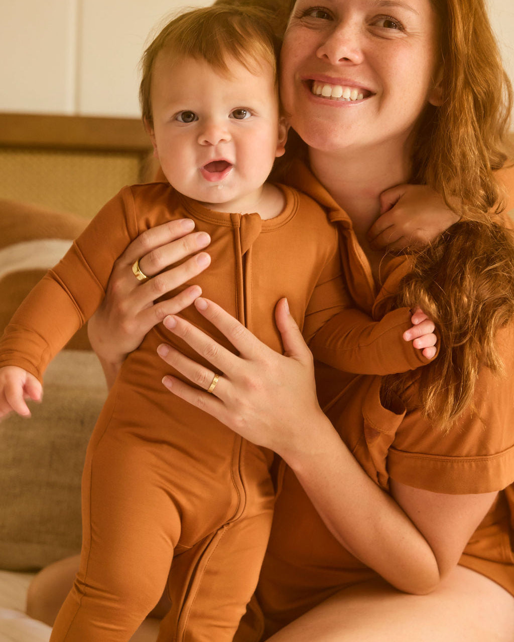 Woman holding a baby in matching Canyon Clay Onesie set indoors.