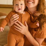 Woman holding a baby in matching terracotta pajama set indoors.