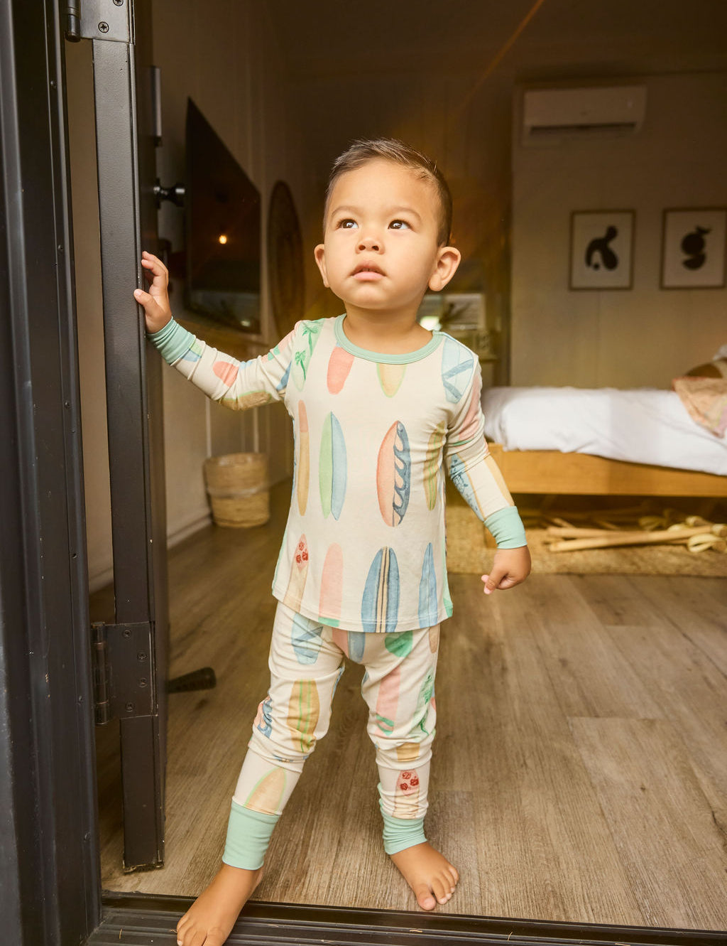 Child in hand-painted surfboard pajamas standing in a doorway with a bedroom in the background