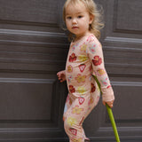 Child in a patterned outfit holding a flower in front of a door