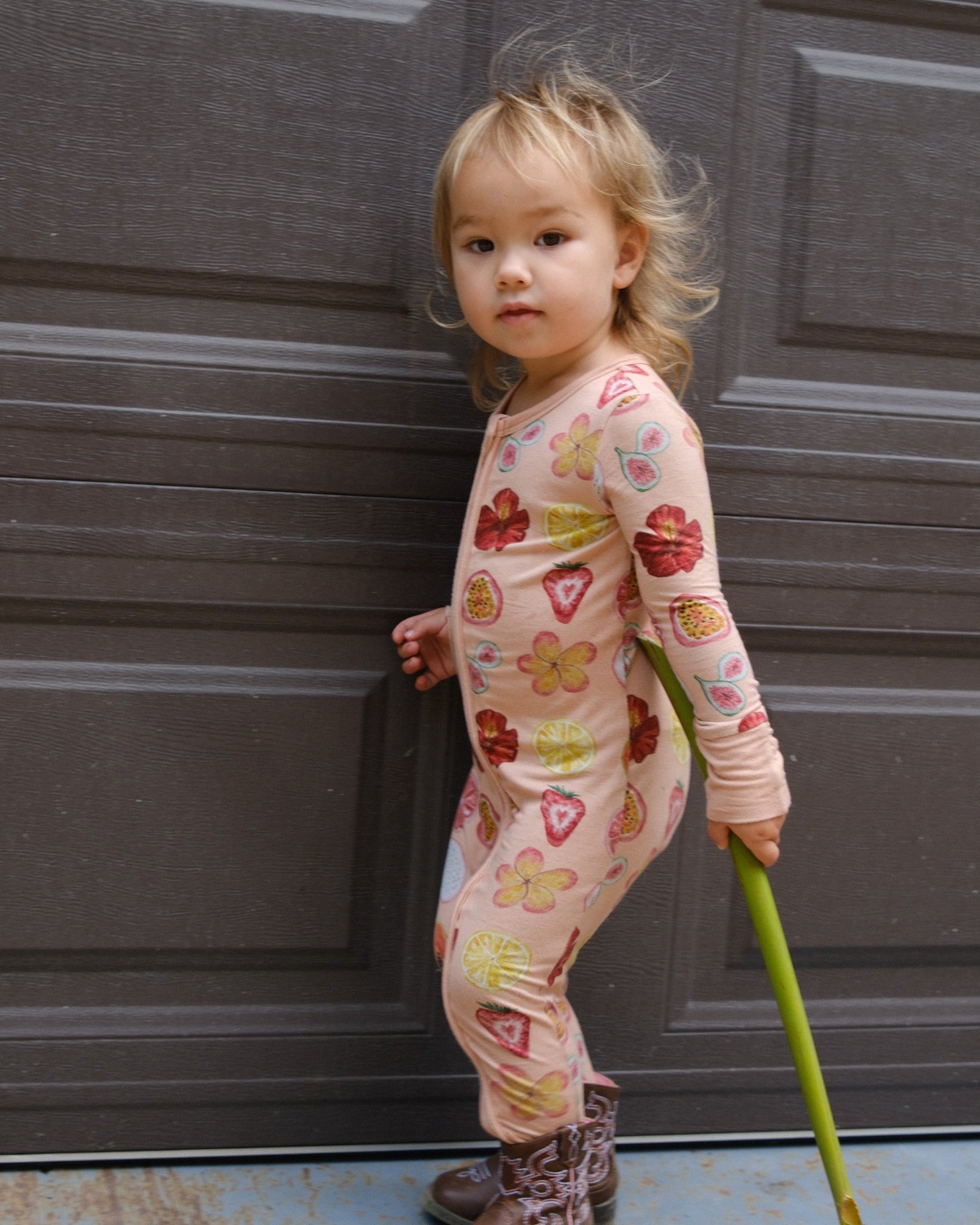 Child in a patterned outfit holding a flower in front of a door