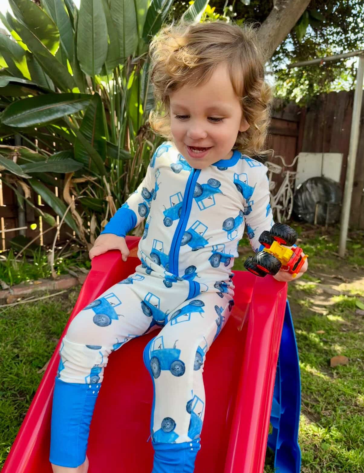 Child in a blue tractor onesie sliding down a red slide outdoors