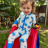 Child in a blue tractor onesie sliding down a red slide outdoors