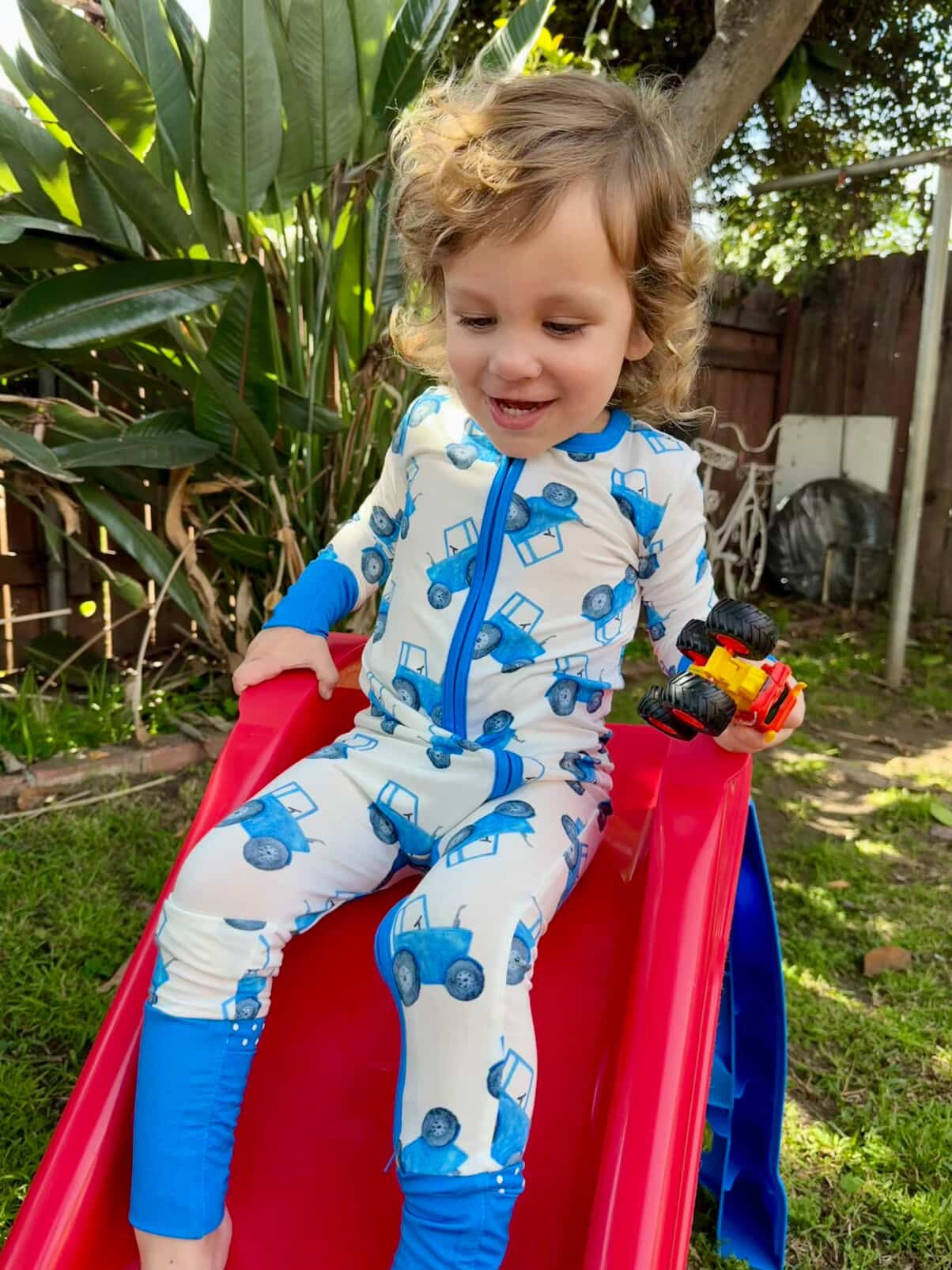 Child in a blue tractor onesie sliding down a red slide outdoors