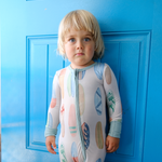 Child wearing a hand-painted surboard onesie standing against a blue door
