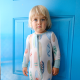 Child wearing a hand-painted surboard onesie standing against a blue door