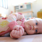 Baby lying on a floor wearing colorful pajamas with a blurred room background