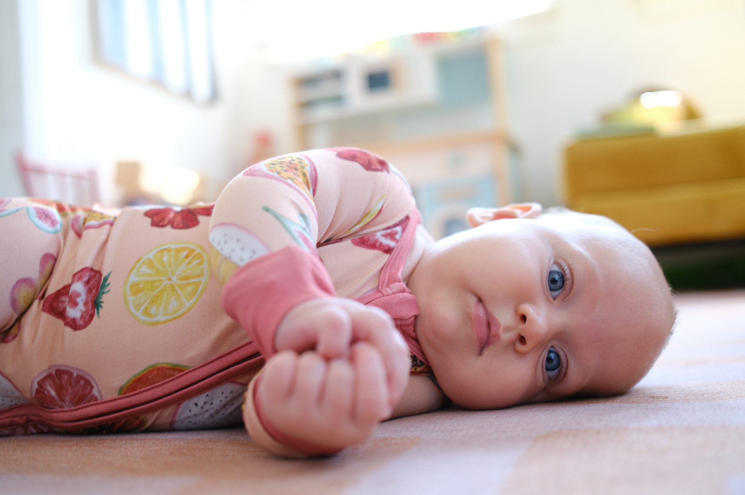 Baby lying on a floor wearing colorful pajamas with a blurred room background
