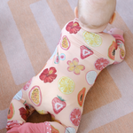 Baby wrapped in a colorful hand-painted onesie with fruit patterns on a striped floor.