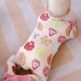 Baby wrapped in a colorful hand-painted onesie with fruit patterns on a striped floor.