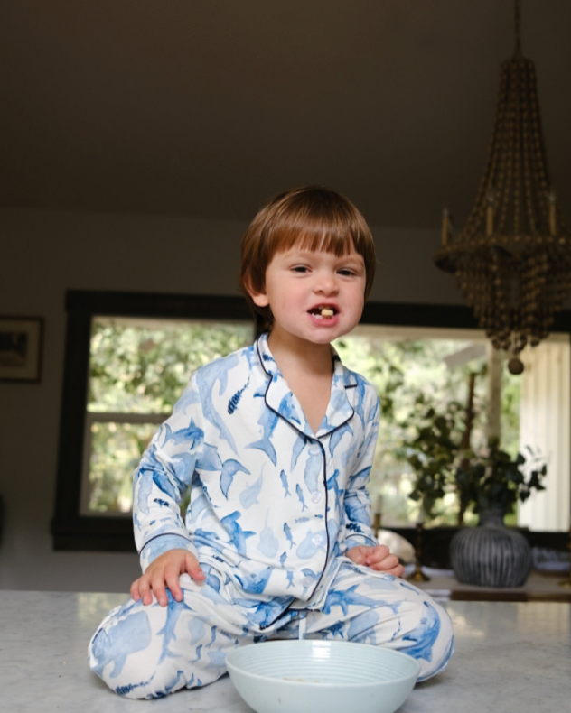 Child in blue floral pajamas sitting on a kitchen counter with a bowl.