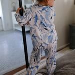 Child wearing a blue shark-patterned onesie standing on a bed.