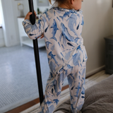 Child wearing a blue shark-patterned onesie standing on a bed.