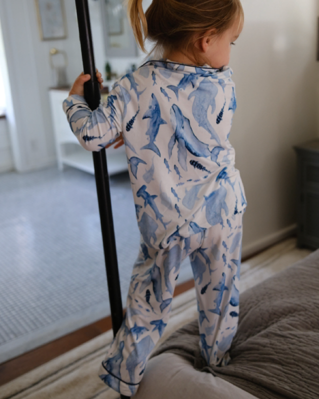 Child wearing a blue shark-patterned onesie standing on a bed.