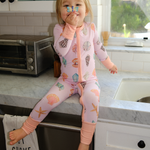 Child in a pink onesie with animal prints sitting on a kitchen counter.