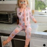 Child in a pink onesie with animal prints sitting on a kitchen counter.
