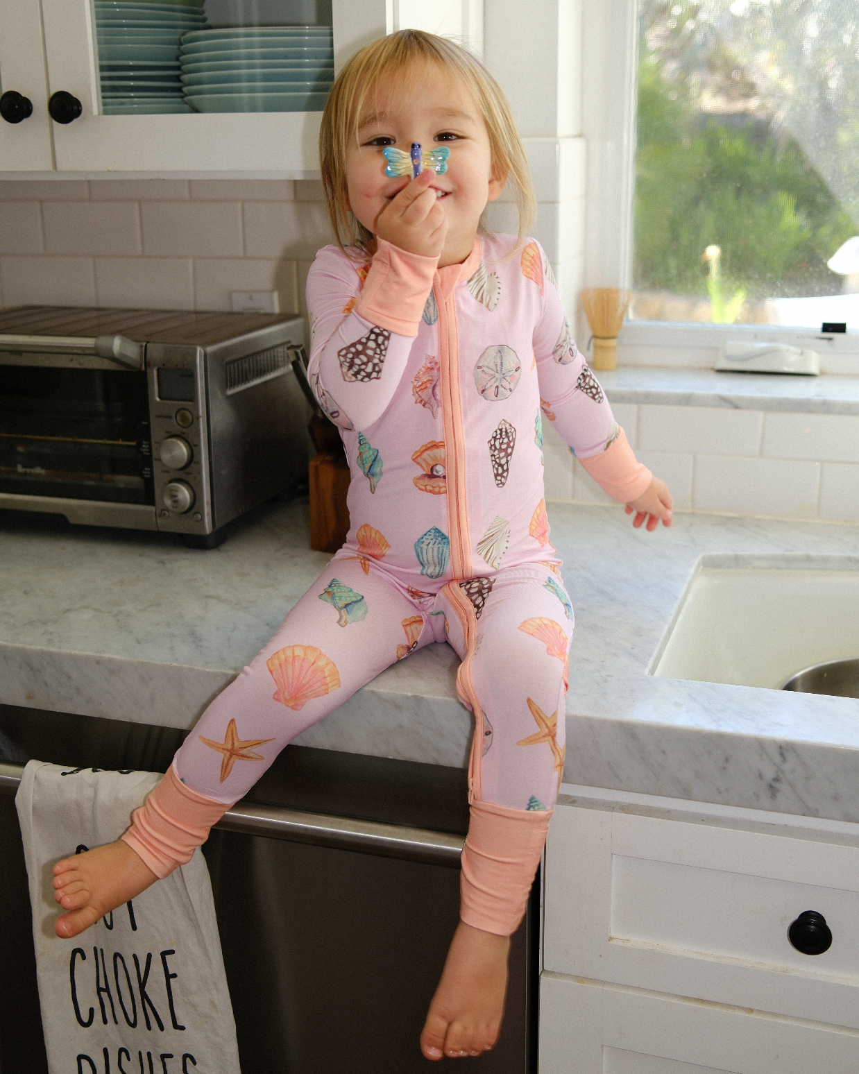 Child in a pink onesie with animal prints sitting on a kitchen counter.