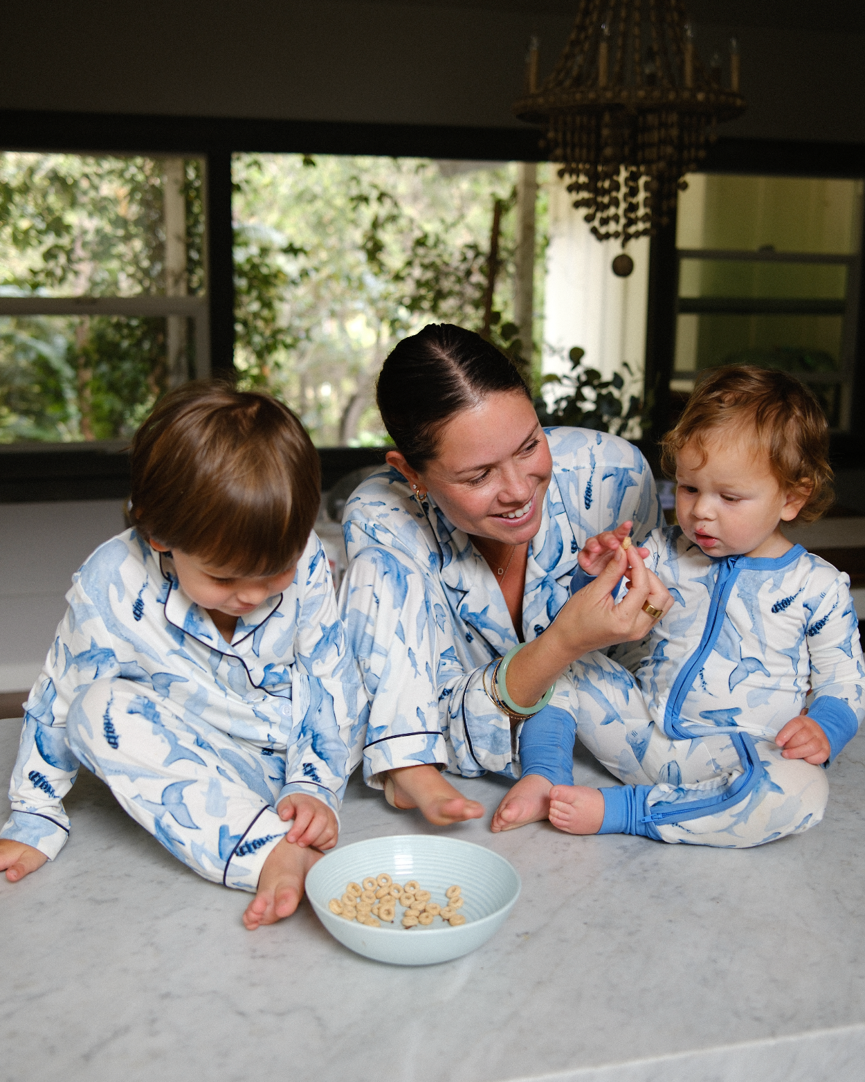 Woman and two children in matching pajamas sitting on a kitchen counter with a bowl of popcorn.